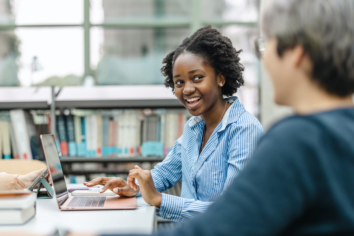 female-teenage-student-talking-with-tutor-in-library